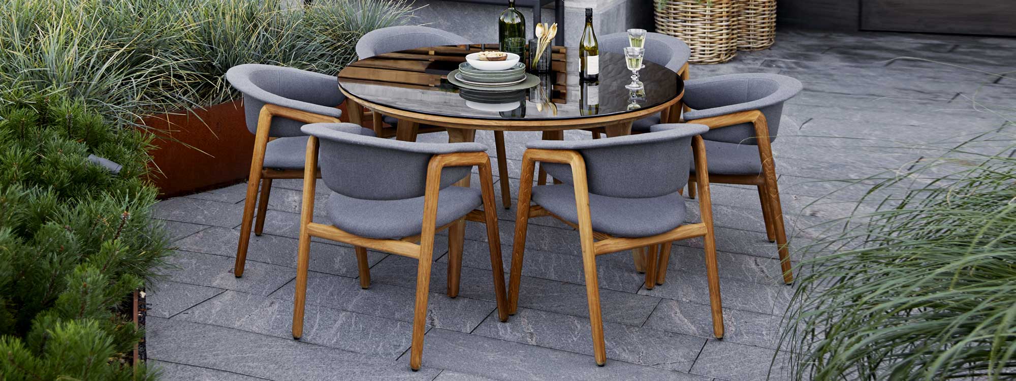 Image of 6 Caneline Luna garden chairs around Aspect circular teak table with Smokey Black toughened glass table top