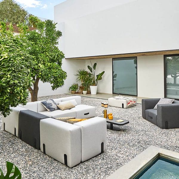Image of grey and light-grey Miami outdoor corner sofa and grey lounge chair in whitewashed courtyard with citrus trees and gravel