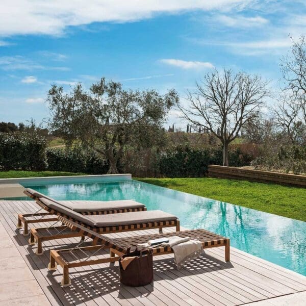 Image of RODA Mistral teak sun loungers with webbed seat and back on horizon poolside with lawn and trees in background