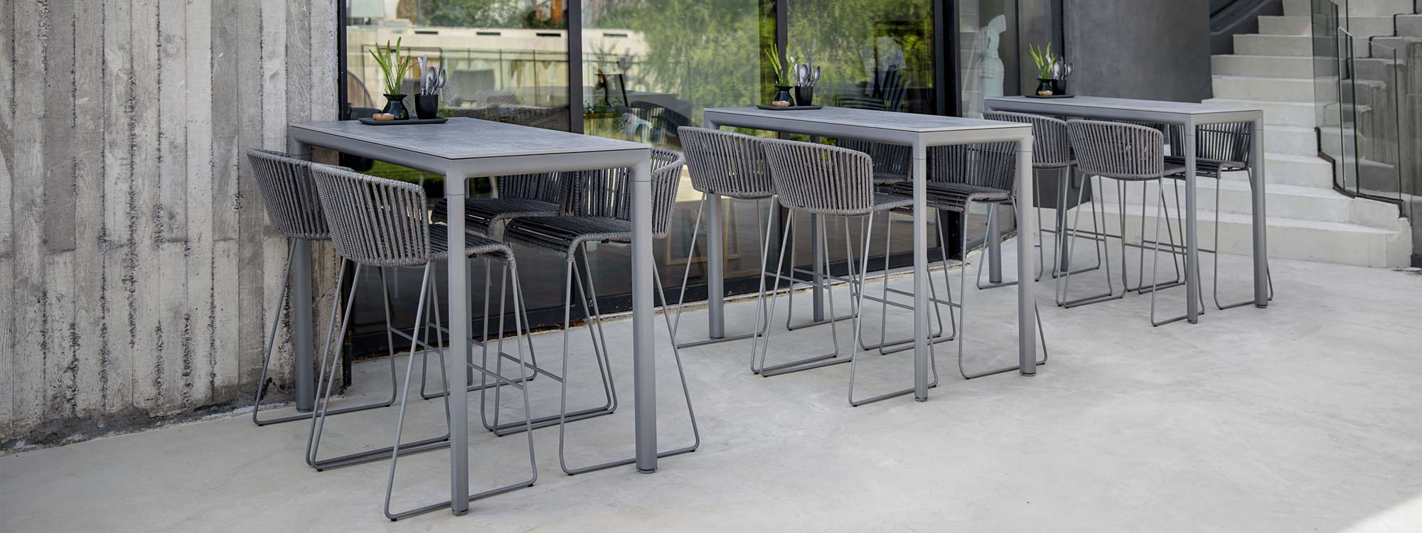 Image of row of grey Drop bar tables and grey bar stools by Cane-line, shown on outdoor terrace