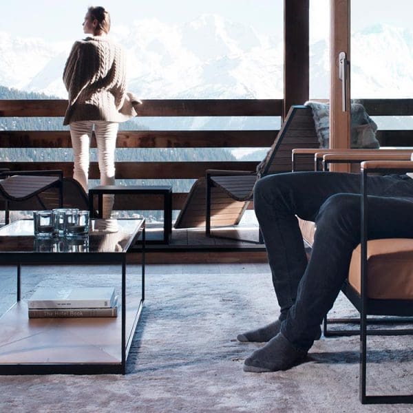 Image of man sat in Monaco interior lounge chair, with Roshults Sun Chairs on balcony outside, with snow-capped mountains in the background