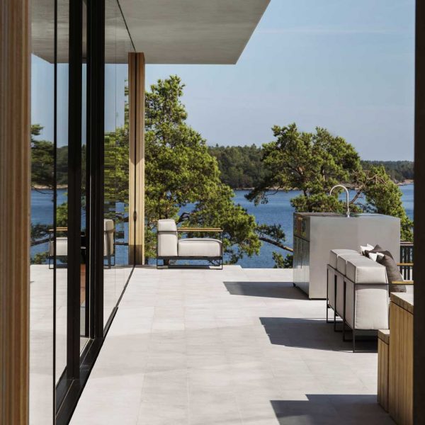Image of Roshults Moore minimalist garden lounge chair on long veranda, with modern glass building to the left and lake and woodland in the background
