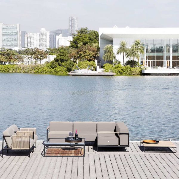 Image of Moore modern outdoor corner sofa and Antibes modern outdoor lounge chairs, shown in decking with lake, buildings and palm trees in the background