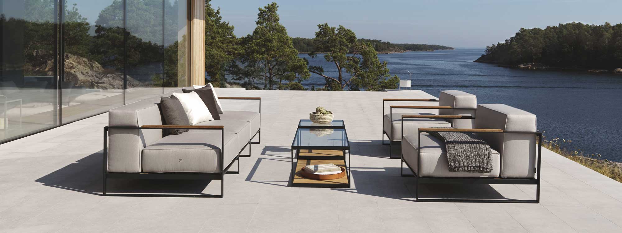 Image of Roshults Moore minimalist garden sofa and lounge chairs on terrace, with Swedish lake and woodland in the background