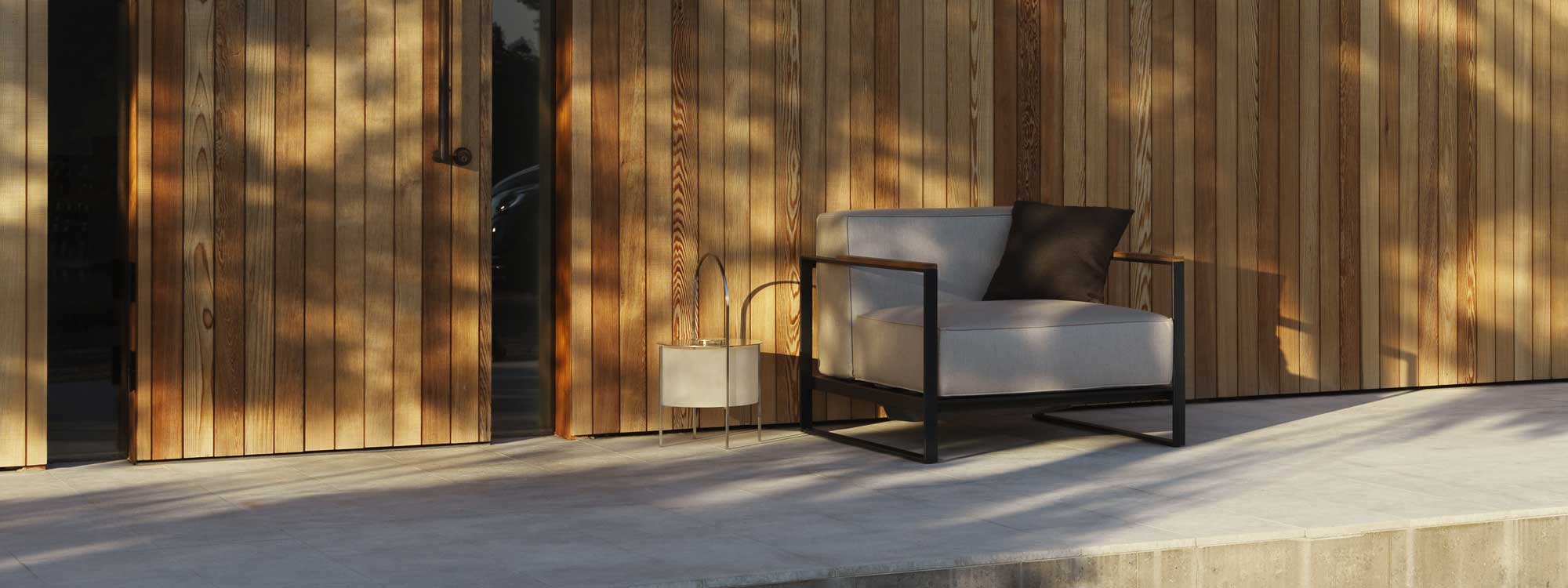 Image of Moore minimalist garden lounge chair in early evening sun, shown on concrete terrace against wooden weatherboarded wall