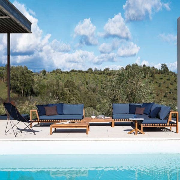 Image of RODA Network modern teak sofa with blue cushions and Lawrence folding wing chair on sunny poolside terrace
