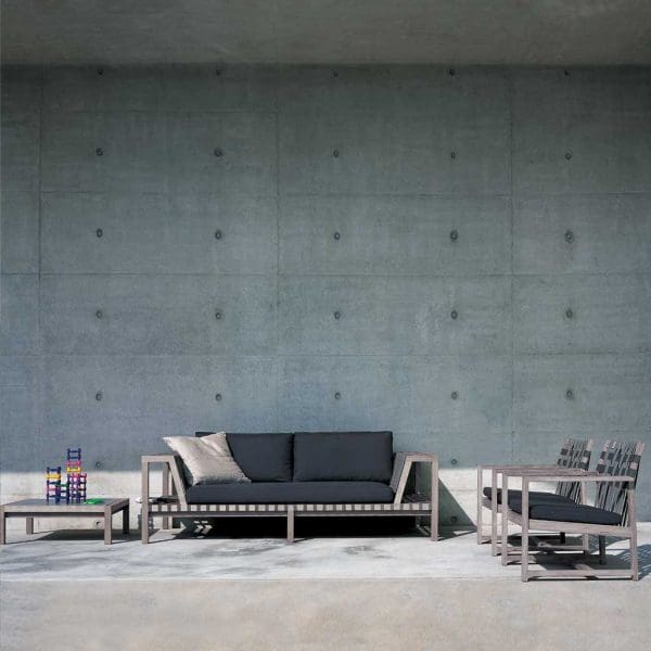 Image of weathered silver-grey Network garden sofa on minimalist poured concrete terrace with concrete wall in background