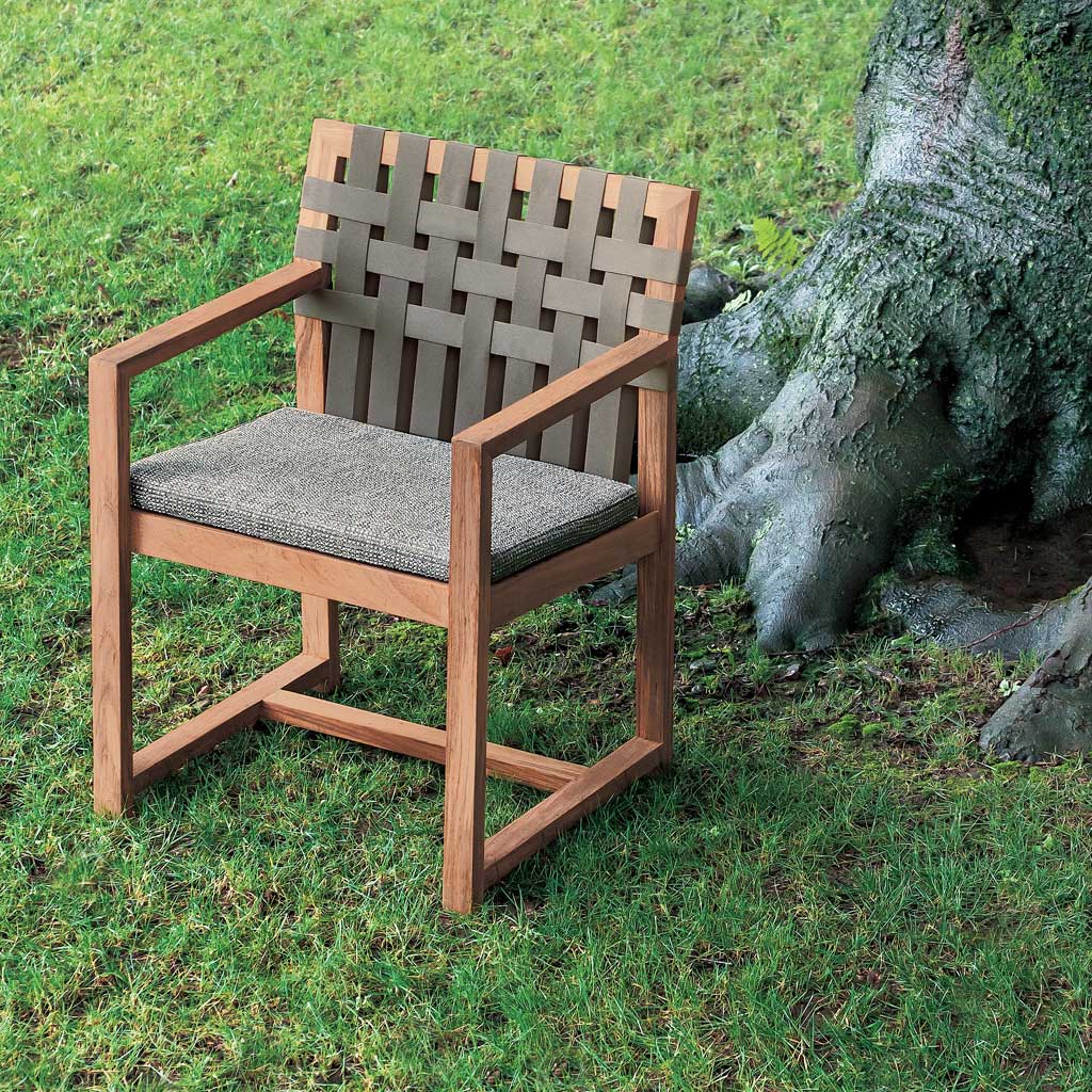 Image of RODA Network teak garden armchair with brown webbed seat and back, next to roots and tree trunk of large tree