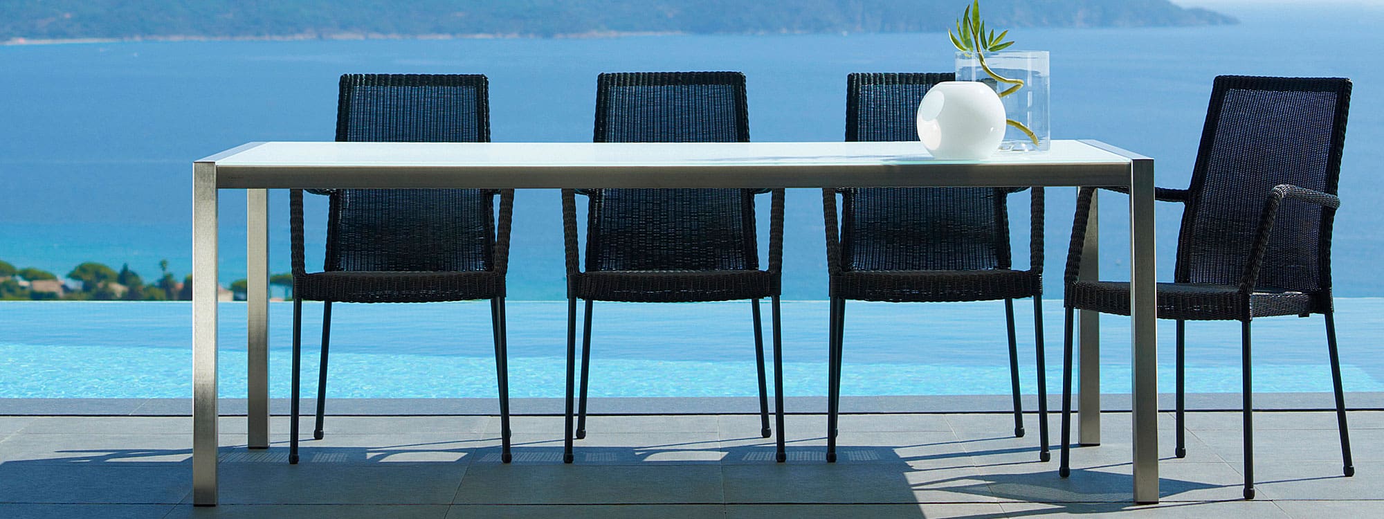 Image of Newport black rattan garden armchairs around Cane-line dining table, shown on poolside
