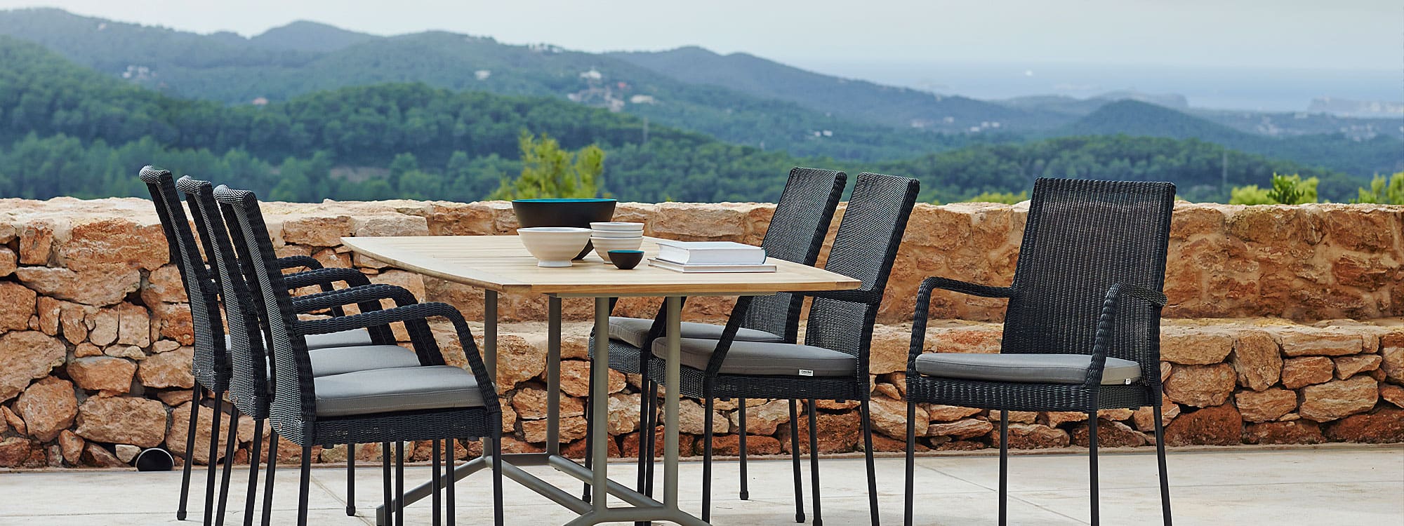 Image of Newport black rattan outdoor armchairs around Cane-line teak garden table, with rolling countryside in background