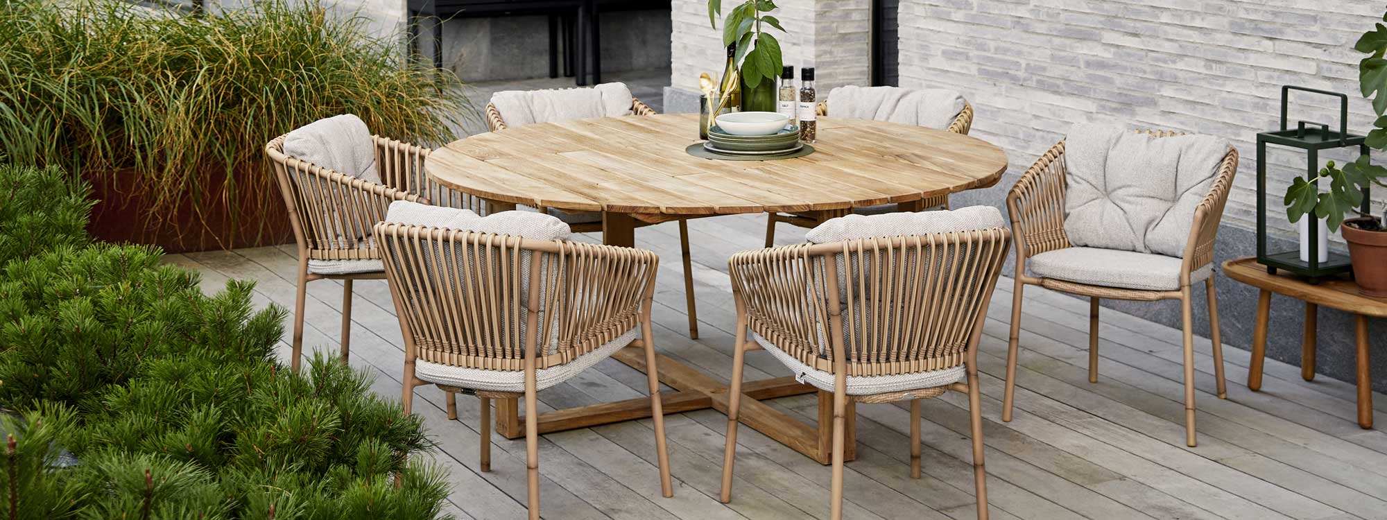 Image of Cane-line Endless round teak table and Ocean bamboo effect chairs, shown on decking surrounded by plants