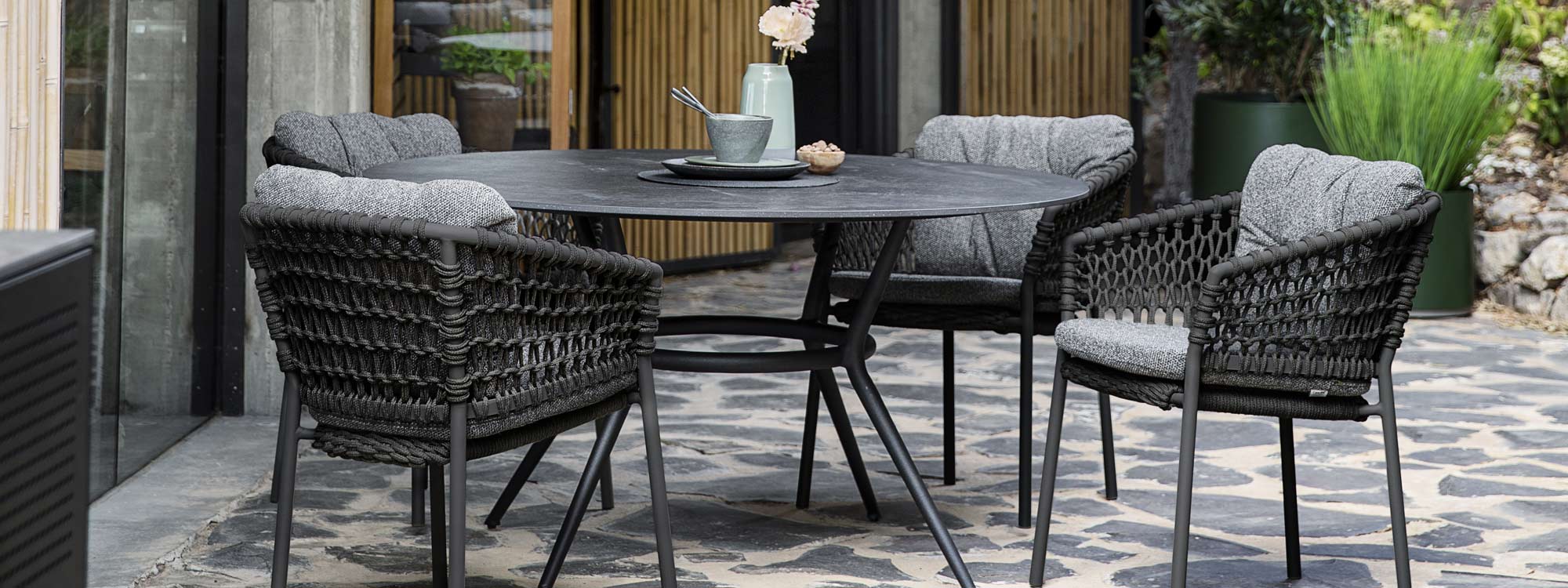 Image of dark grey Ocean garden chairs around Joy circular dining table with black fossil ceramic top by Caneline
