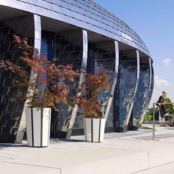 Image of Octa architectural outdoor plant pots by Flora, shown on sunny terrace outside modern curvaceous building