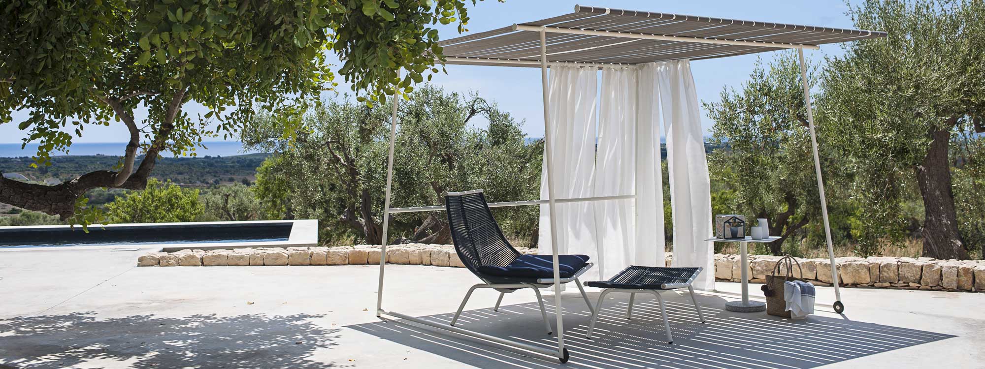 Image of milk-colored Ombrina modern pergola and Laze garden chair and foot rest by RODA, shown on sunny Italian terrace
