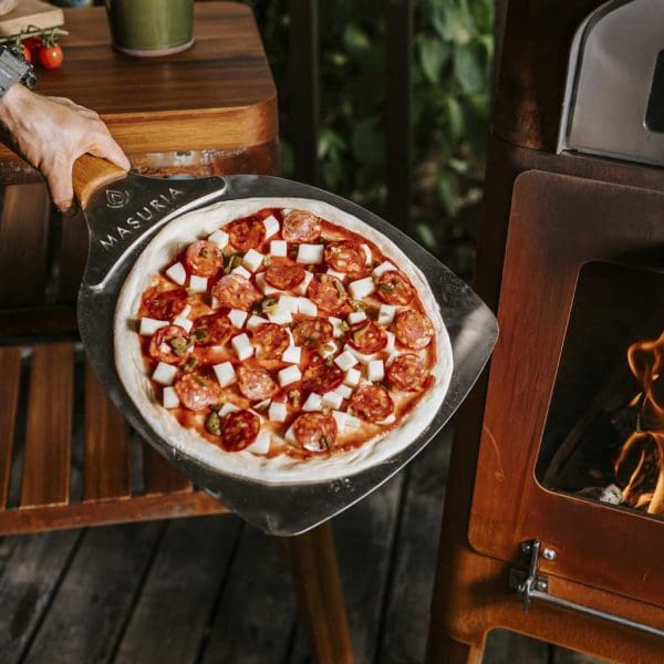 Image of pizza on a pizza paddle about to be cooked in M-Classic pizza oven