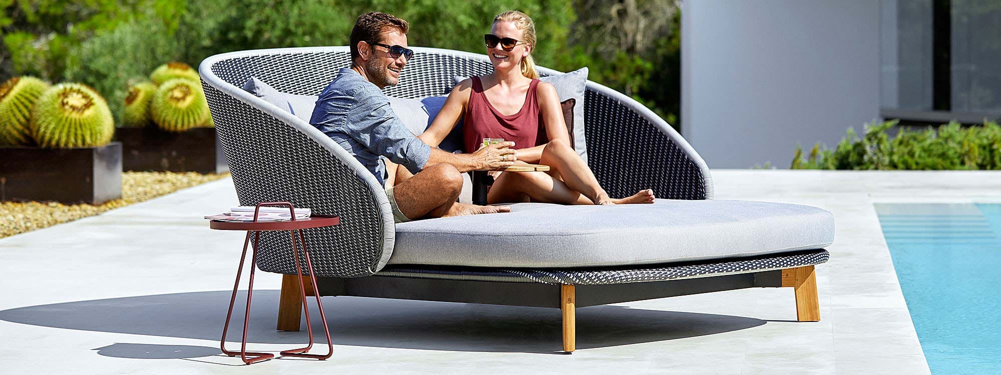 Image of couple relaxing in Cane-line Peacock twin daybed on sunny poolside