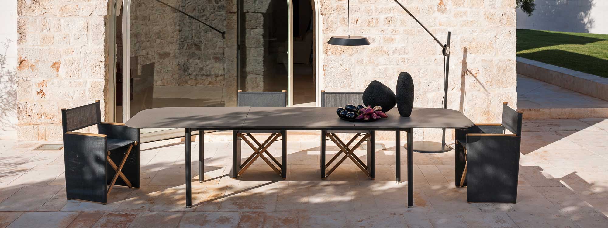 Image of RODA Piper extending garden table and Orson modern director chairs in light and shade of rustic Italian courtyard