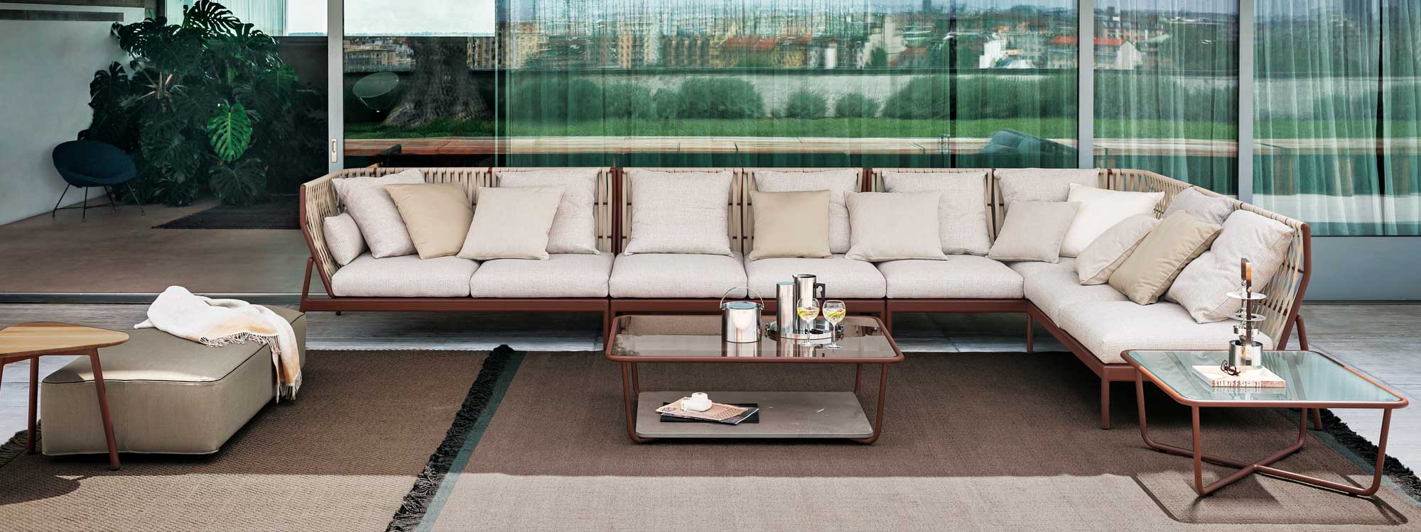 Image of Piper large outdoor corner sofa with rust-colored frame and taupe cushions by RODA, shown on terrace covered with outdoor rugs