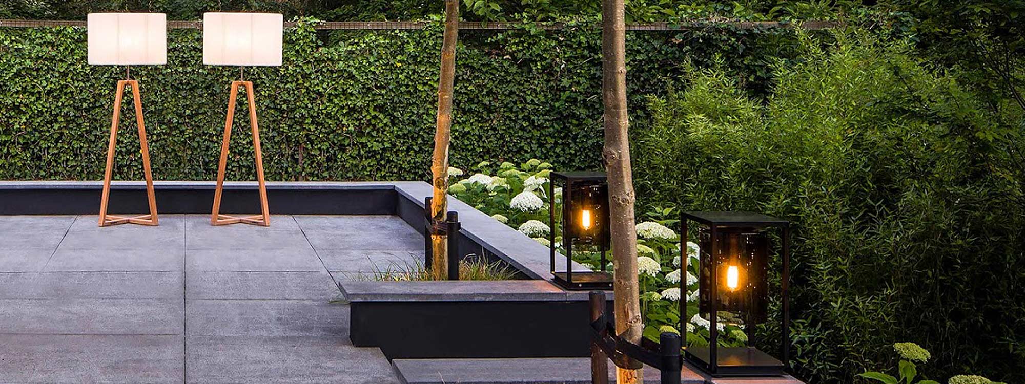 Image of pair of illuminated Dome Gate modern garden lights on either side of terrace steps, with Club garden floor lamps by Royal Botania in the background