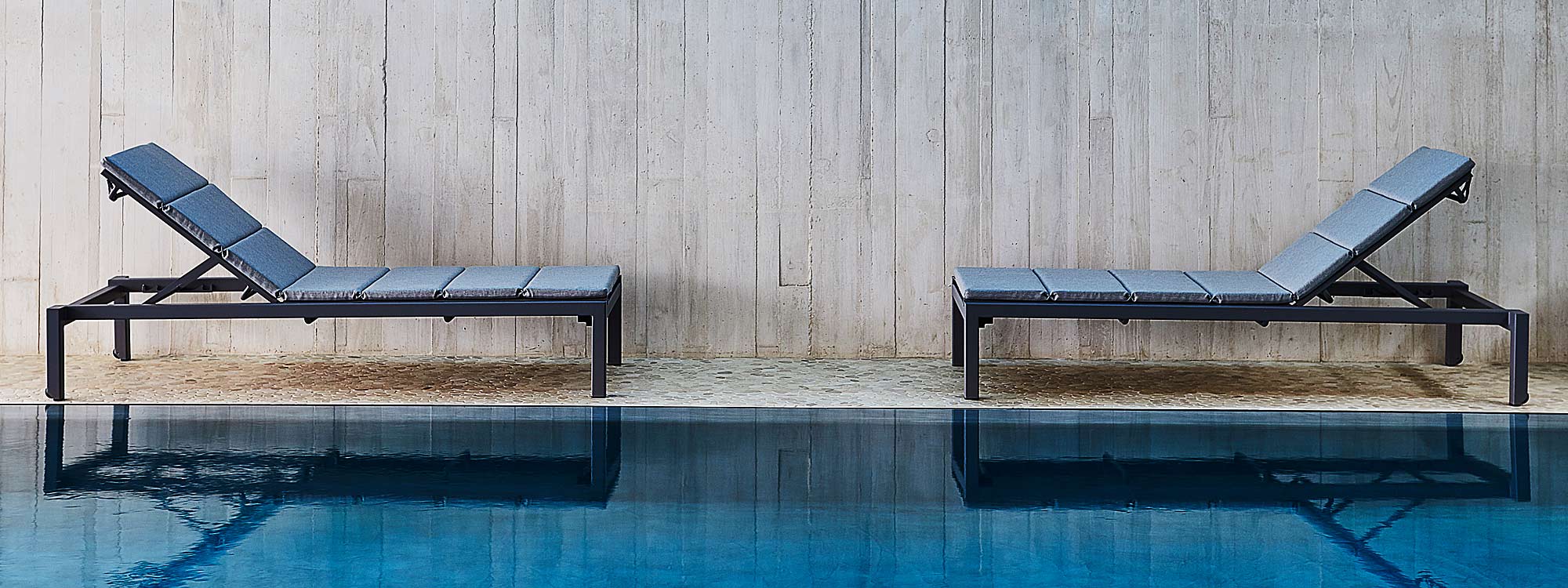 Image of pair of Cane-line Relax modern sun beds on poolside in front of poured concrete wall