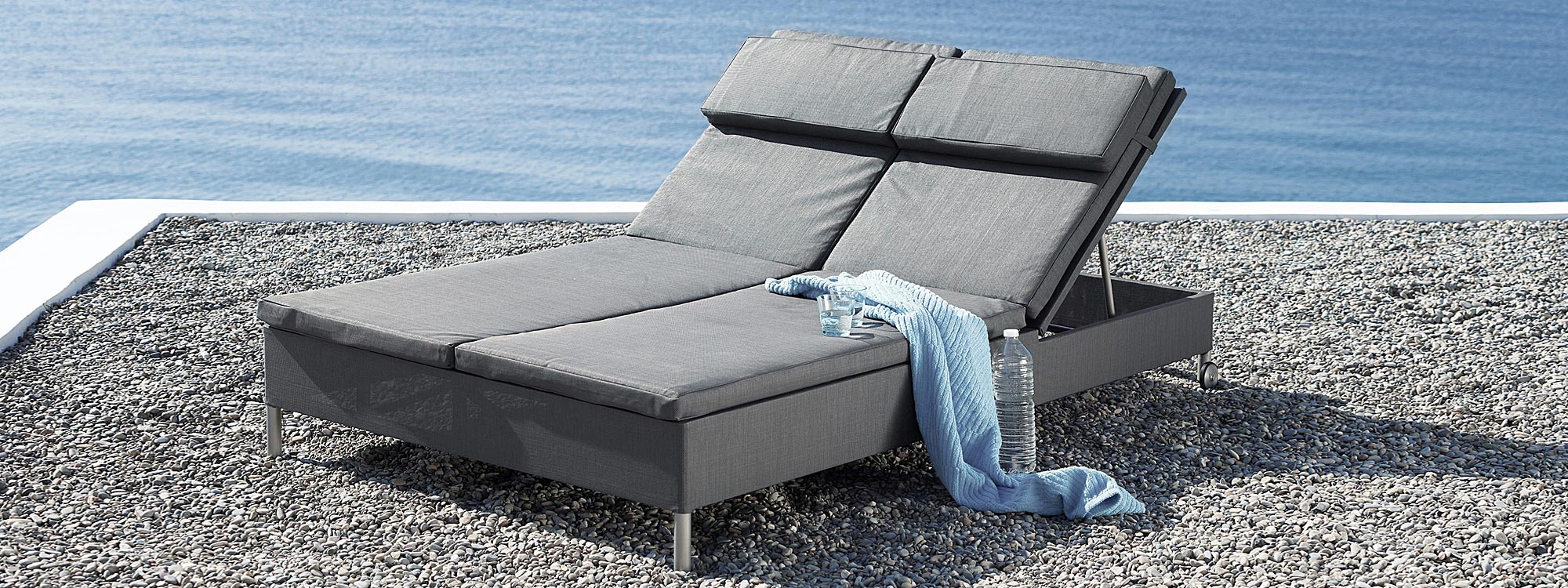 Image of Caneline Rest twin sunbed with grey cushions, on gravel terrace above sea