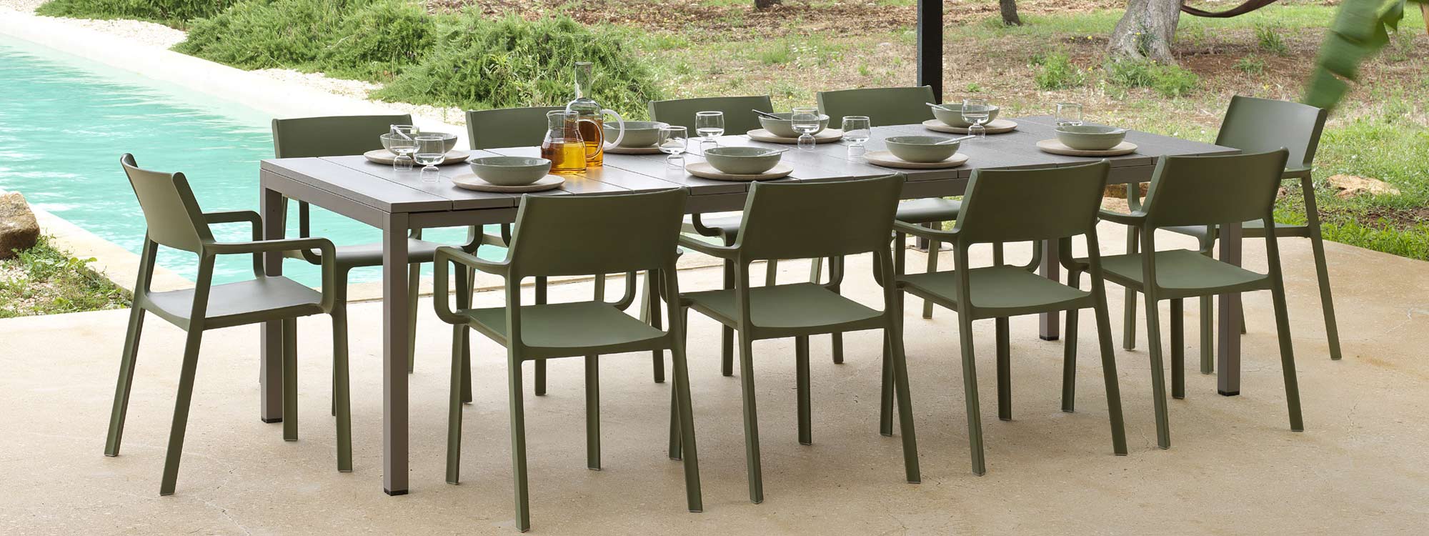 Image of Rio taupe garden table and agave coloured Trill garden chairs by Nardi, with olive trees and lawn in the background