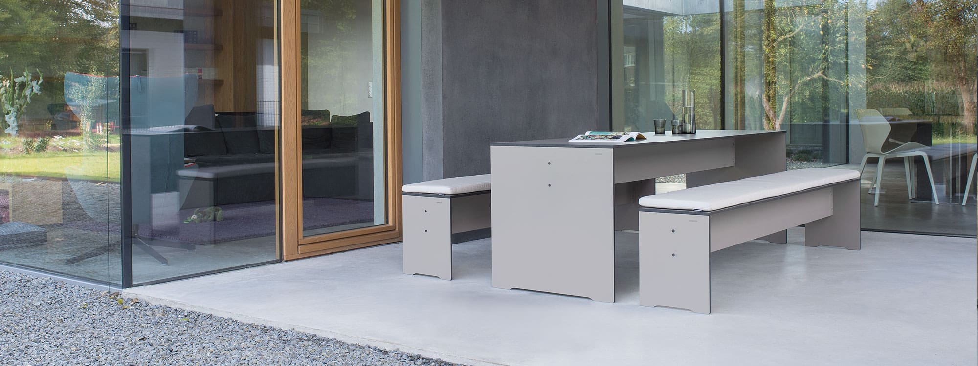 Image of Taupe RIVA modern garden table and benches on modern concrete terrace with floor to ceiling windows in the background
