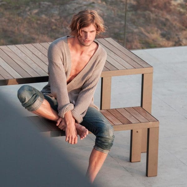 Image of man in jeans and cardigan sat on Roshults minimalist garden bench without back
