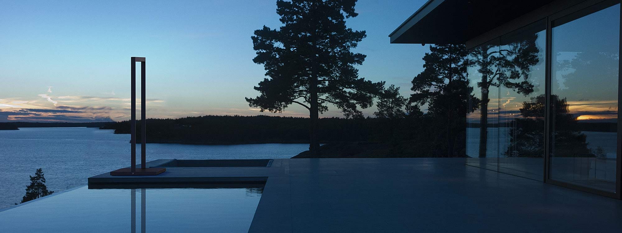 Image at dusk of Roshults modern garden shower on terrace, with lakes and woodland in the background