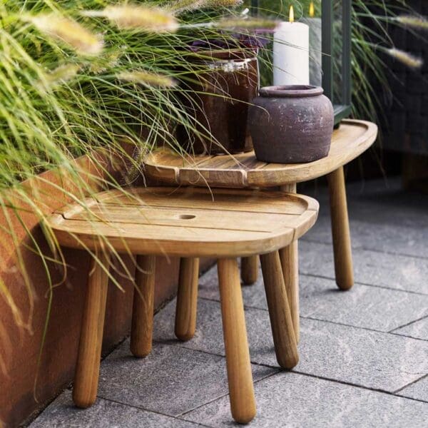 Image of nest of Royal Teak low tables by Caneline, shown against rusted steel raised bed with grasses inside