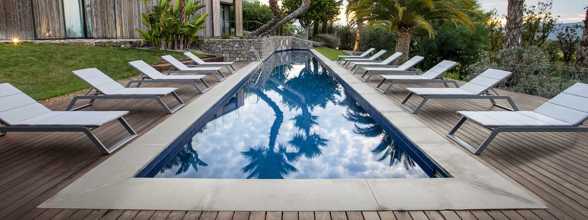 Striking image of Siesta sun loungers by Cane-line down either side of swimming pool at dusk