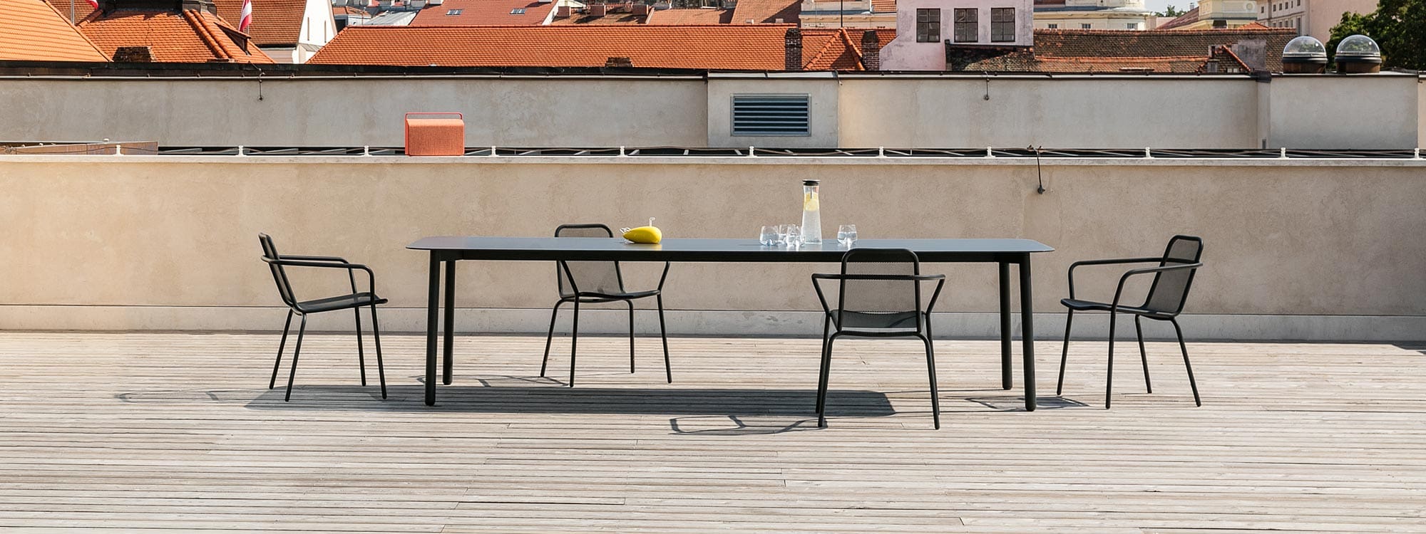 Image from side of Starling long garden table and outdoor dining chairs in anthracite stainless steel, with rooftops in the background