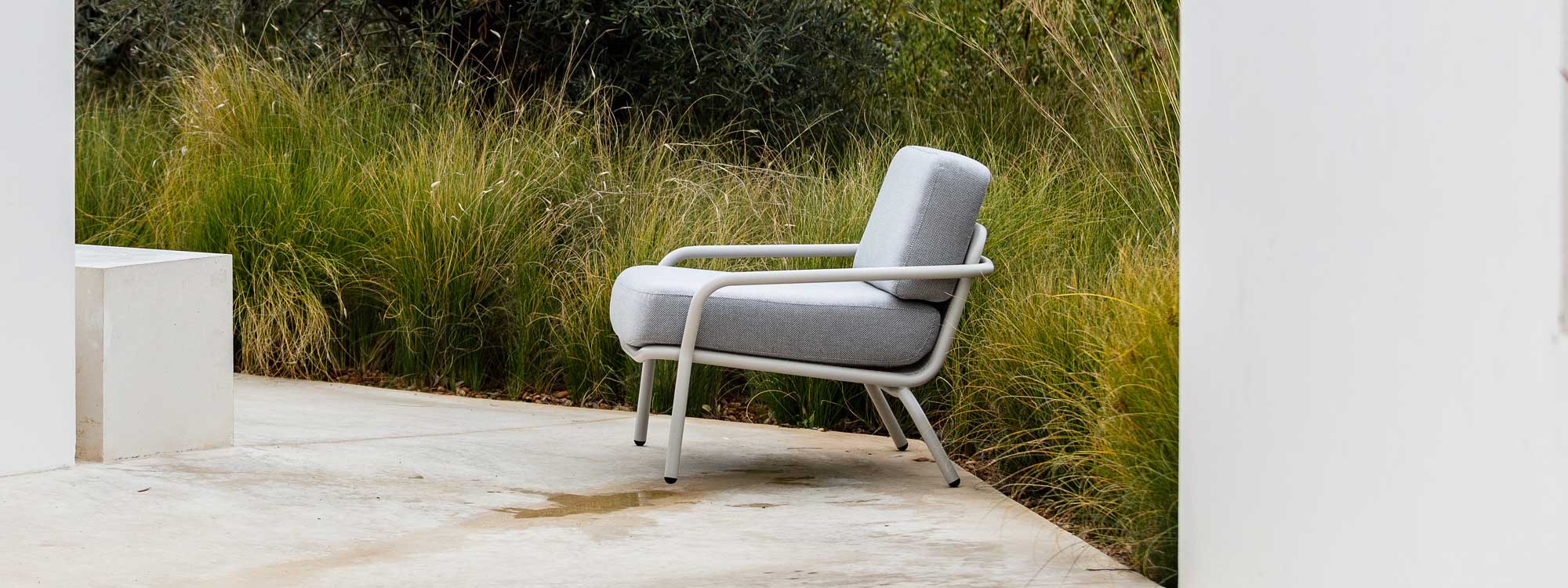 Image of white Starling modern outdoor relax chair with White frame and Grey cushions in front of ornamental grasses