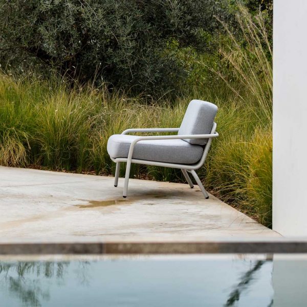 Image of Starling white garden easy chair with grey cushion on poolside surrounded by architectural grasses