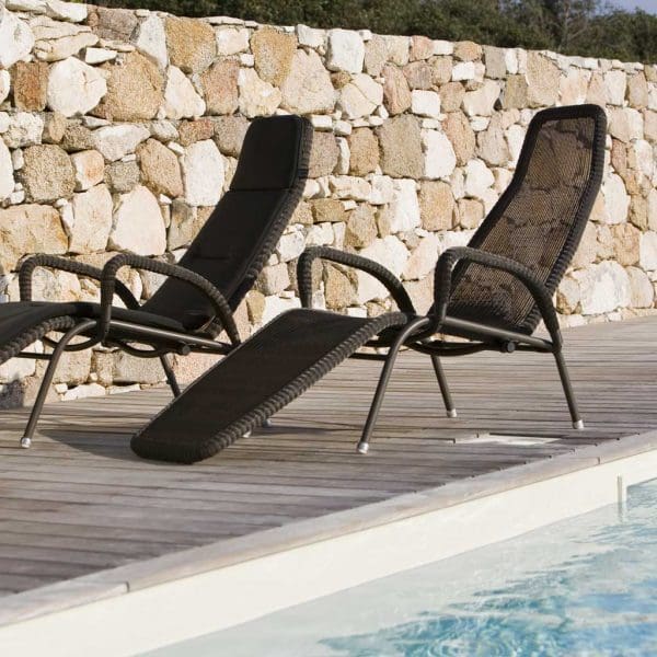 Image of pair of Sunrise reclining relax chairs by Caneline, shown next to swimming pool with dry stone wall in the background