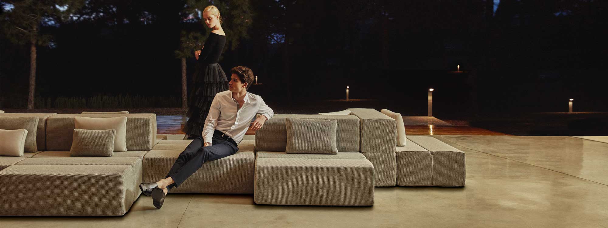 Image of couple sat on and around Vondom Tablet modular garden lounge furniture, with illuminated garden in the background