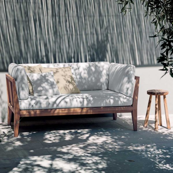 Image of courtyard in sun and shade with RODA Teka 2 seat garden sofa with white cushions, with split-cane screening in the background