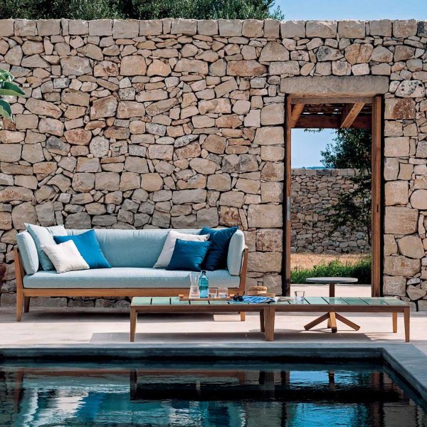 Image of RODA Teka large teak garden sofa with light blue cushions, next to Teka teak low table with ceramic glazed top, on sunny rural Italian poolside