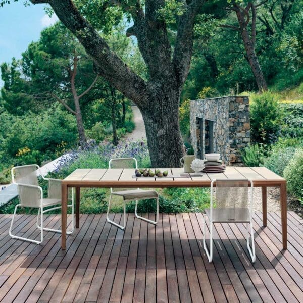 Image of RODA Teka rectangular garden table with Harp white garden chairs on decking, with trees and lavender in background