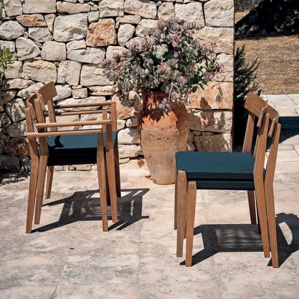 Image of stacked Teka contemporary teak dining chairs by Rodaonline, on sunny Italian terrace