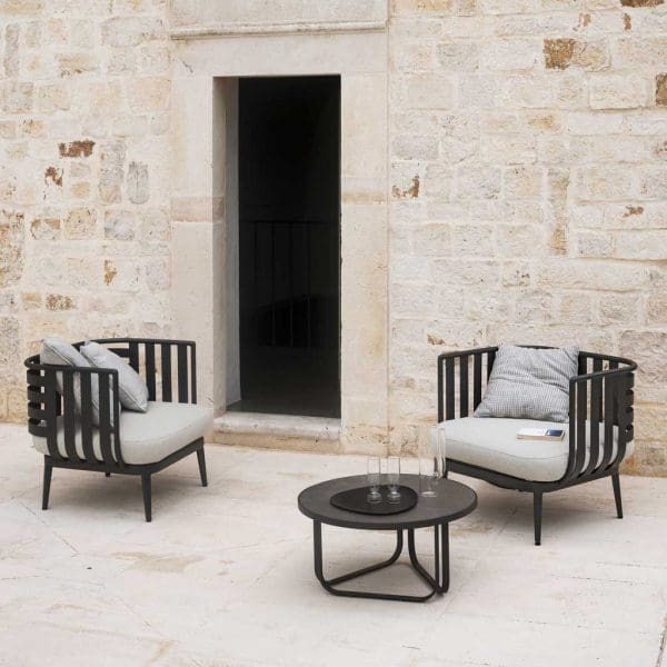 Image of 2 Thea aluminum garden lounge chairs and round low table by RODA, against stone wall with open door
