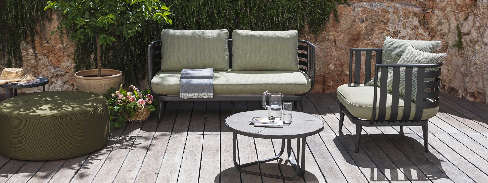 Image of RODA Thea aluminum garden sofa, lounge chair and low tables with Double round garden pouf against rustic stone wall