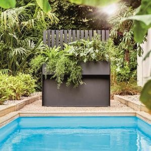 Image of Ticino raised planter and trellis in grey HPL, planted with exotic plants, located on poolside with more plants in the background