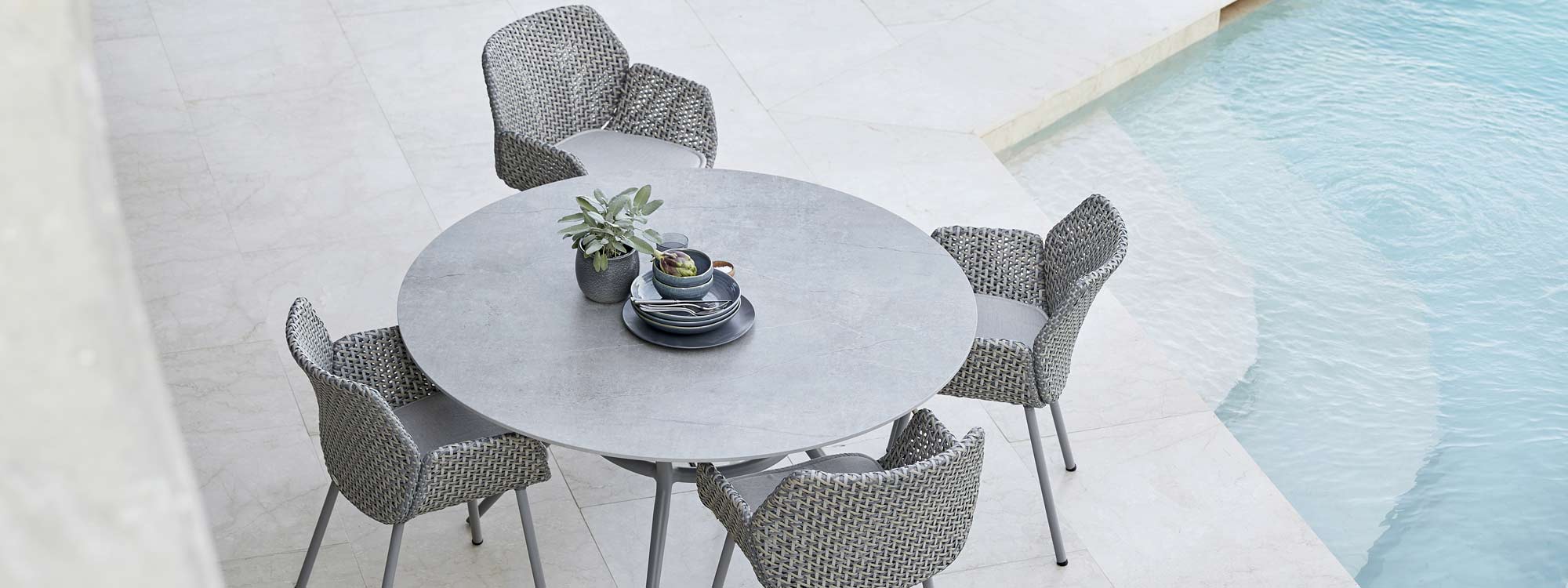 Image of Vibe rattan chairs around Cane-line Joy circular garden table, shown in sleek modern poolside