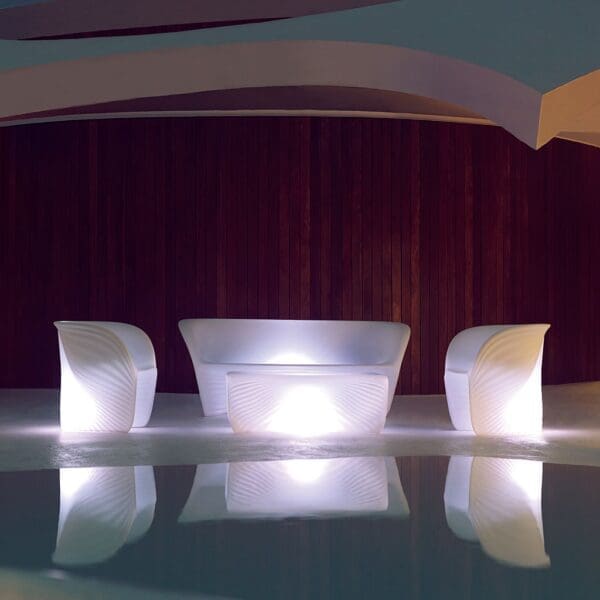 Nighttime image of Vondom Biophilia modernist outdoor lounge furniture with white LED illumination, reflected in water of swimming pool in foreground