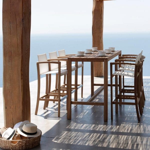 Image of XQI teak bar table and high chairs by Royal Botania on terrace in dappled shade of pergola