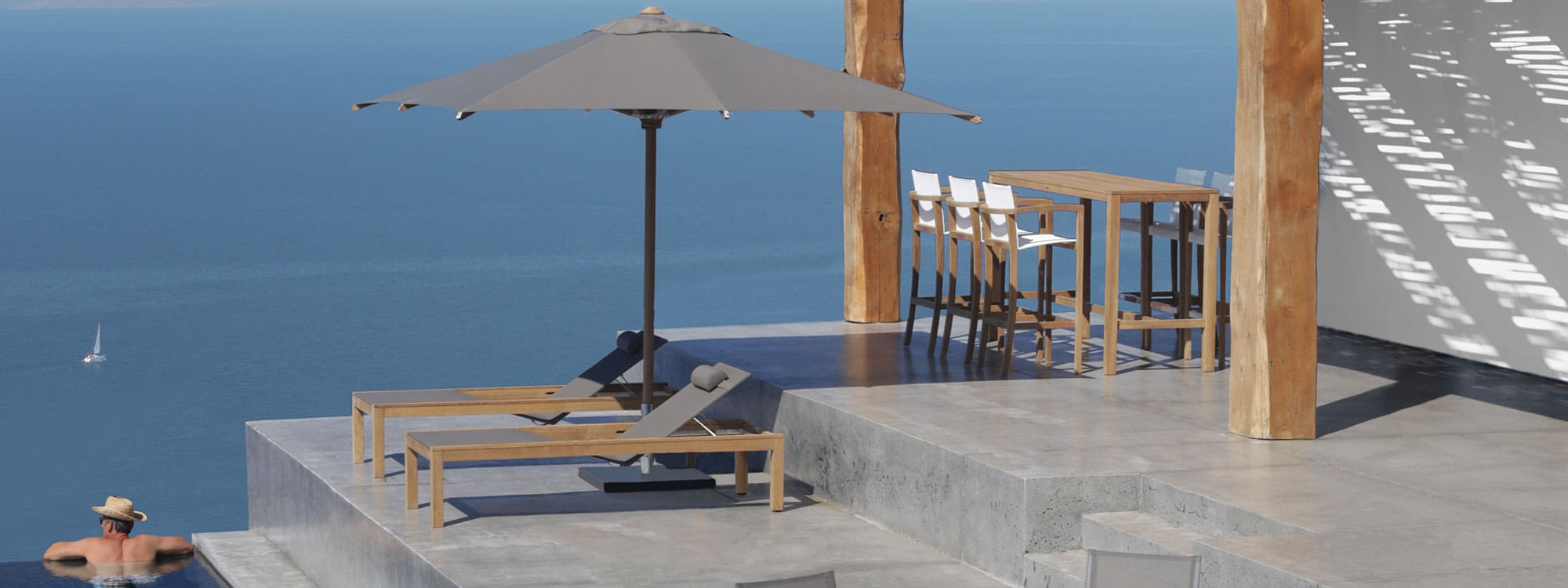 Image of XQI teak sun loungers and bar set by Royal Botania on terrace high above sparkling Mediterranean sea