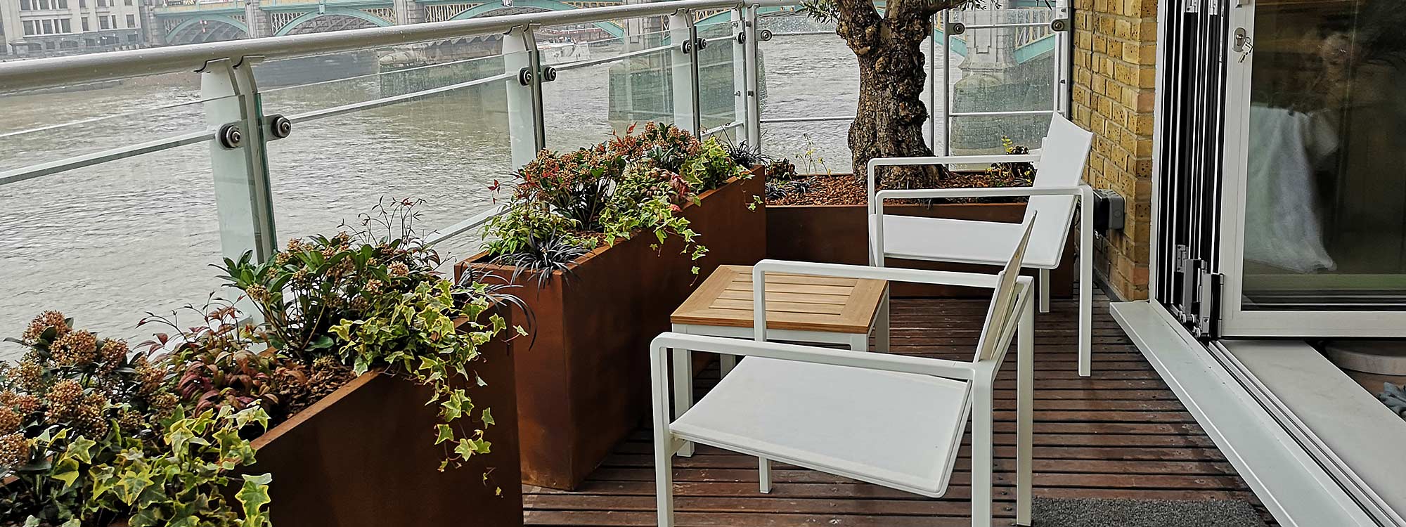 Photo of chic white and teak outdoor low seats and table on modern London balcony