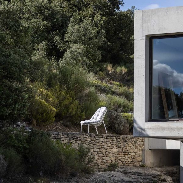 Image of white Todus Albus garden lounge chair and cushion, shown on terrace with house to one side and steep planted hillside in background