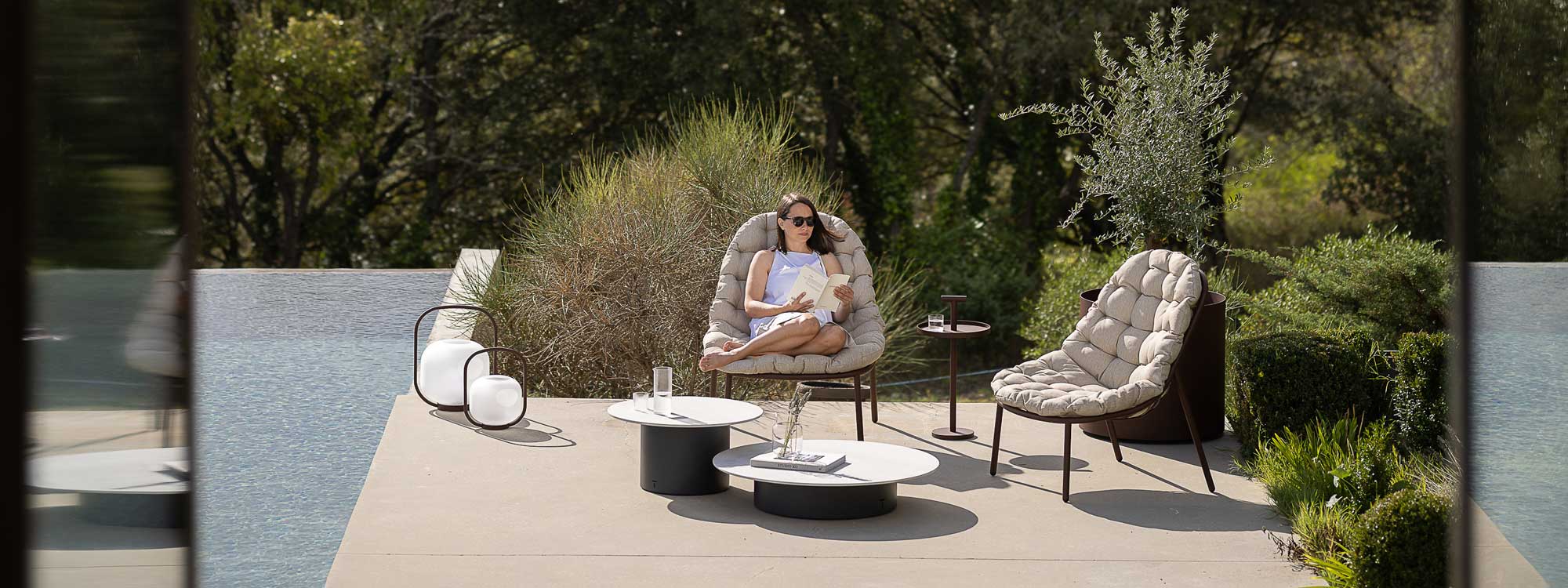 Image of woman sat in Albus modern outdoor relax chair on poolside, with Branta low tables in front of her and Albus garden side table to one side
